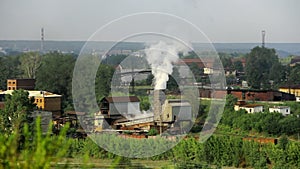 Pipes of industrial plant smoke among green trees and nature in Alapaevsk.