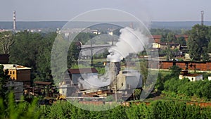 Pipes of industrial plant smoke among green trees and nature in Alapaevsk.