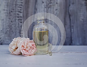 Pipette and the bottle of rose oil lies on the wooden table in the garden next to the delicate pink fragrant flowers