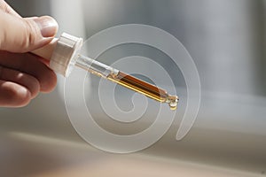 Pipette with serum or cosmetic liquid close-up in hand in soft focus on brown background. Soothing cbd oil. Alternative
