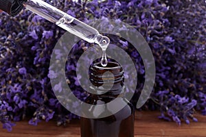 Pipette dropping essential oil into a glass bottle on lavender background. Close up