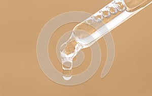 Pipette with essential oil, serum with peptides, emulsion, hyaluronic acid on beige background. Closeup of beige dropper