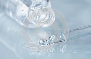 Pipette with fluid hyaluronic acid and opened bottle on blue background. Cosmetics and healthcare concept closeup