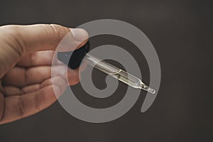 Pipette with serum or cosmetic liquid close-up in hand in soft focus on brown background.