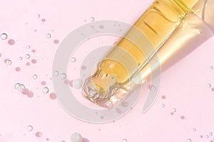 Pipette with serum or liquid yellow gel on light pink glass background. Beauty cosmetic concept. Top view