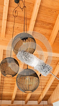 Pipidastr wipes dust from metal lamps.Ceiling lights cleaning.fluffy bristle brush cleans lamps under a wooden ceiling.