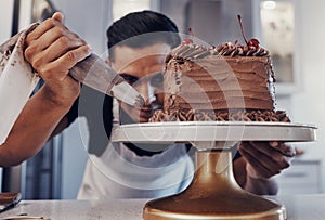 Piping, chef and man baker baking a cake with chocolate in a kitchen or pastry cook preparing a sweet recipe. Food