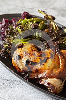 Piri or Peri chicken dinner with roasted broccoli and pickled red cabbage on a black plate.