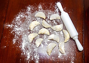 Pirogues ,pierogis, verenik, on wooden table with rolling pin and wheat flour scattered