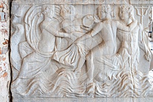 Close-up on classic sculptures carved in a marble wall representing a group of young naked people interacting
