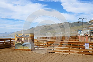 Pismo Beach sign on the pier and wooden boardwalk. Beautiful view of Pismo Beach city with mountains and cloudy sky on background