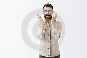 disstressed and annoyed adult hipster guy with long beard in black trendy glasses and beige jacket frowning