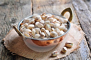 Pistachio in a copper bowl on the old wooden background photo
