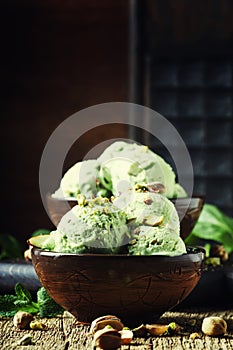 Pistachio ice cream with nuts, decorated with mint leaves, vintage wooden background, selective focus