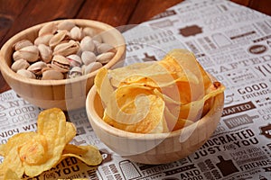 Pistachio nuts, and potato chips in wooden bowls on craft paper.