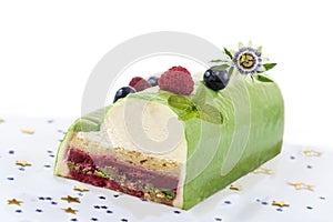 Pistachio Raspberry Yule Log decorated with fresh raspberries, blueberry, and pasion flower on white background.