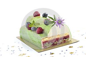 Pistachio Raspberry Yule Log decorated with fresh raspberries, blueberry, and pasion flower on white background.