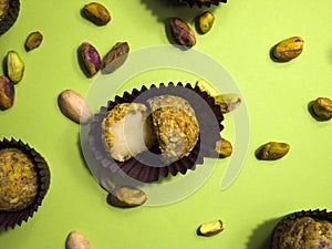 Pistachio white chocolate truffle cut in two halves in a brown candy wrapper on a light green background.