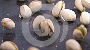 Pistachios slow motion falling on authentic black structured surface.