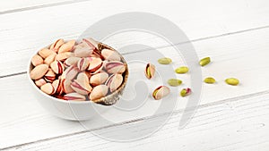 Pistachios in small porcelain bowl, a few peeled green ones on white boards desk next