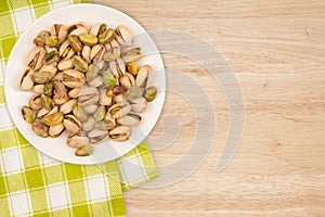 Pistachios in a white plate on a wooden table.