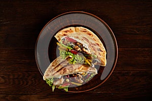 Pita stuffed with chicken, beans and letucce on clay plate over wooden background, side view, selective focus.