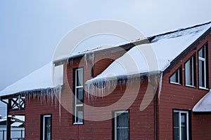 Pitched roof of wooden house covered by snow and icicles