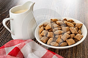 Pitcher with baked milk, napkin, breakfast cereals with filling in bowl on wooden table
