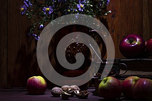 A pitcher of flowers, old books and apples on a wooden background