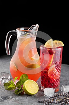 Pitcher with glass of cold lemonade with raspberries lime and mint on gray table on dark background