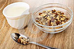 Pitcher with yogurt, bowl of granola with banana and chocolate, spoon with muesli on table