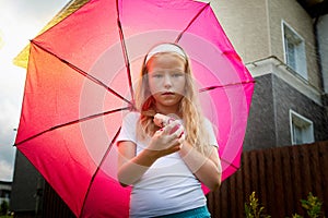 Pity blonde child with pink umbrella under the summer rain with su. Girl enjoying rainfall. Kid playing on the nature