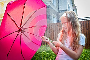 Pity blonde child with pink umbrella under the summer rain with su. Girl enjoying rainfall. Kid playing on the nature