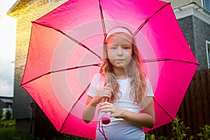 Pity blonde child with pink umbrella under the summer rain with su. Girl enjoying rainfall. Kid playing on the nature