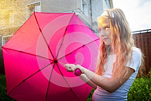 Pity blonde child with pink umbrella under the summer rain with su. Girl enjoying rainfall. Kid playing on the nature