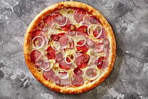 Pizza with bacon slices, salami, hunting sausages, jalapeno and onions on gray background