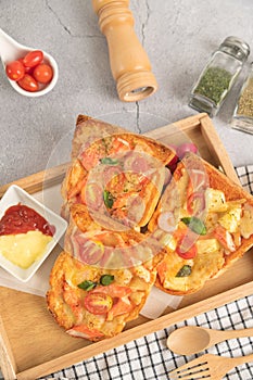 Pizza bread topped with shrimp, crab sticks, tomatoes, sausage, cheese in a wooden tray