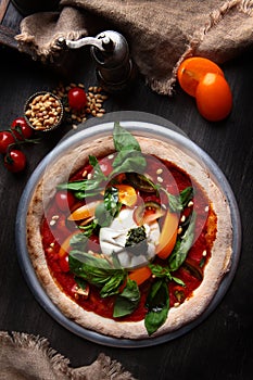 Pizza with burrata cheese and pine nuts. Italian pizza. Metal plate for serving. Green basil leaves. Vertical photo. View from