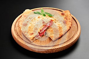 Pizza calzone with basil leaves close up on wooden round board cutted with tomato cheese and ham photo