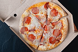 Pizza in a cardboard box on a black chalkboard background. View from above. Pizza delivery. Pizza menu