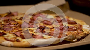 Pizza carnivor made of bacon, sausage and ham. Fast-food photography detail view of a pizza in a delivery box. Home delivered food