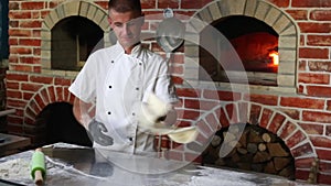 Pizza chef tossing pizza dough in the air in a traditional pizzeria kitchen
