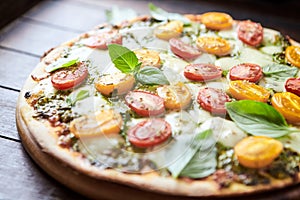 Pizza with cherry tomatoes, mozzarella and basil pesto. Dark wooden background.