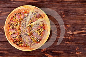 Pizza with chicken breast, corn, bacon and mushrooms, with a slice slightly removed on a wood plate which is on wood