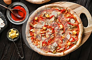 Pizza with chicken meat, cheese, bell pepper, mushrooms and pineapple on black wooden background. Fast food lunch for picnic