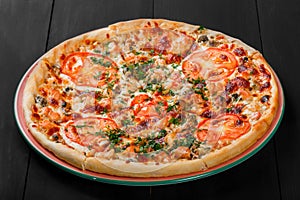 Pizza with chicken, tomatoes, mushrooms, greens and cheese on dark wooden background. Homemade pizza