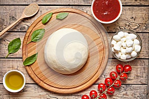 Pizza cooking ingredients on cutting board. Dough, mozzarella, tomatoes, basil, olive oil, spices. Work with the dough