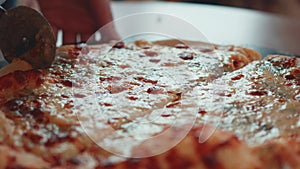 The pizza is cut into several pieces. Delicious juicy pizza is cut with a round knife. Delicious healthy food. Italian