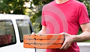 A pizza delivery man holds pizza boxes near the car outdoor. Mockup. Selective focus