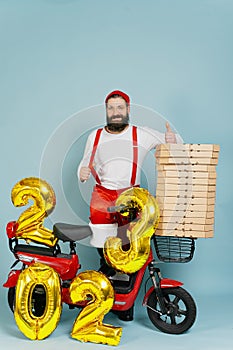 Pizza delivery man in a santa costume and suspenders showing a thumbs up gesture on the background of a red electro moped with the